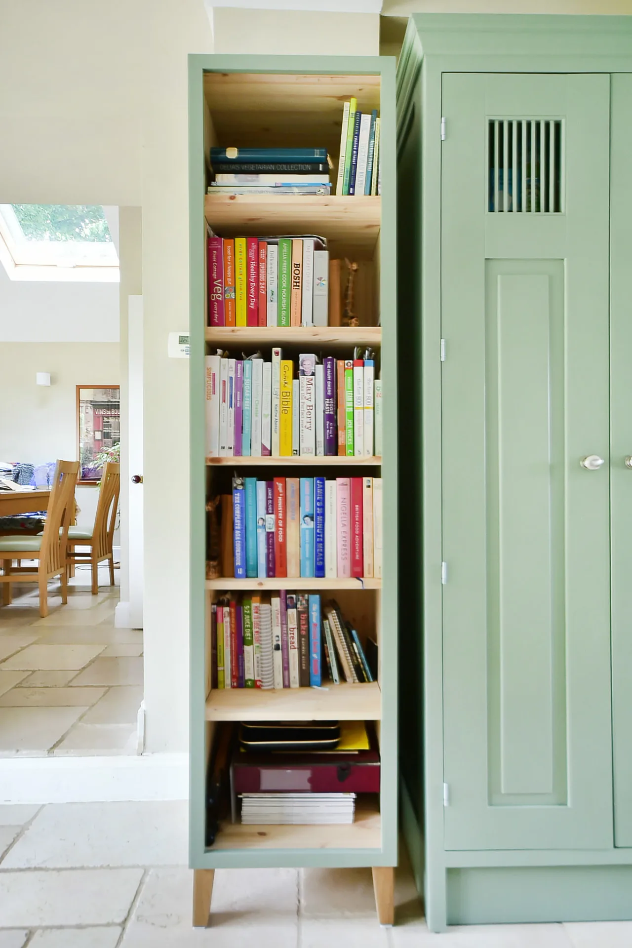 Bespoke sage green painted shelving unit filled with cookery books beside a matching tall cabinet