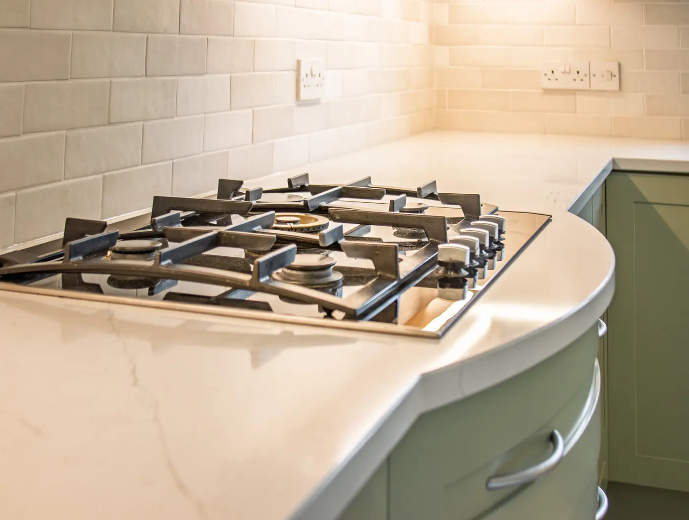 Gas hob set into a curved white quartz worktop with a tiled splashback