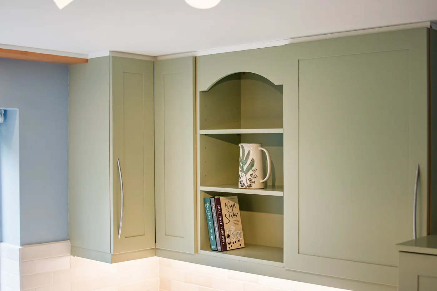 Sage green shaker wall cabinets with an arched open display shelf