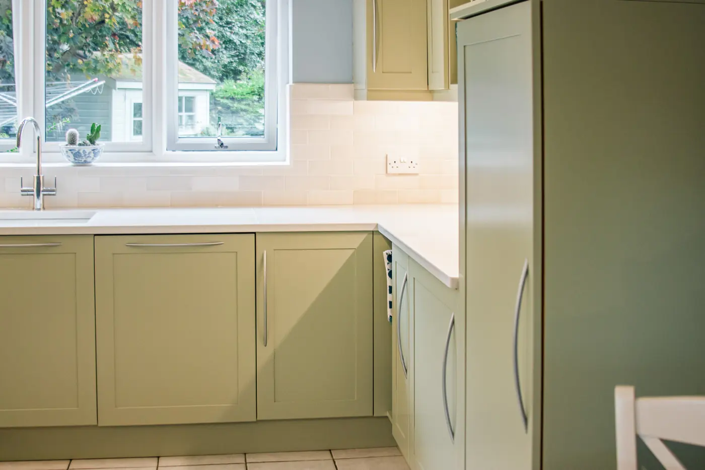 Sage green shaker base units and tall larder cabinet beside the sink run