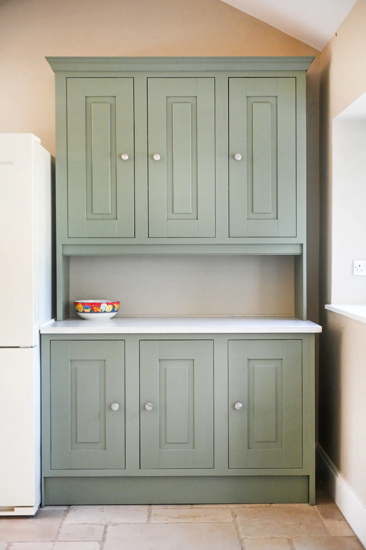Bespoke sage green painted dresser with white worktop, panelled doors and a decorative bowl