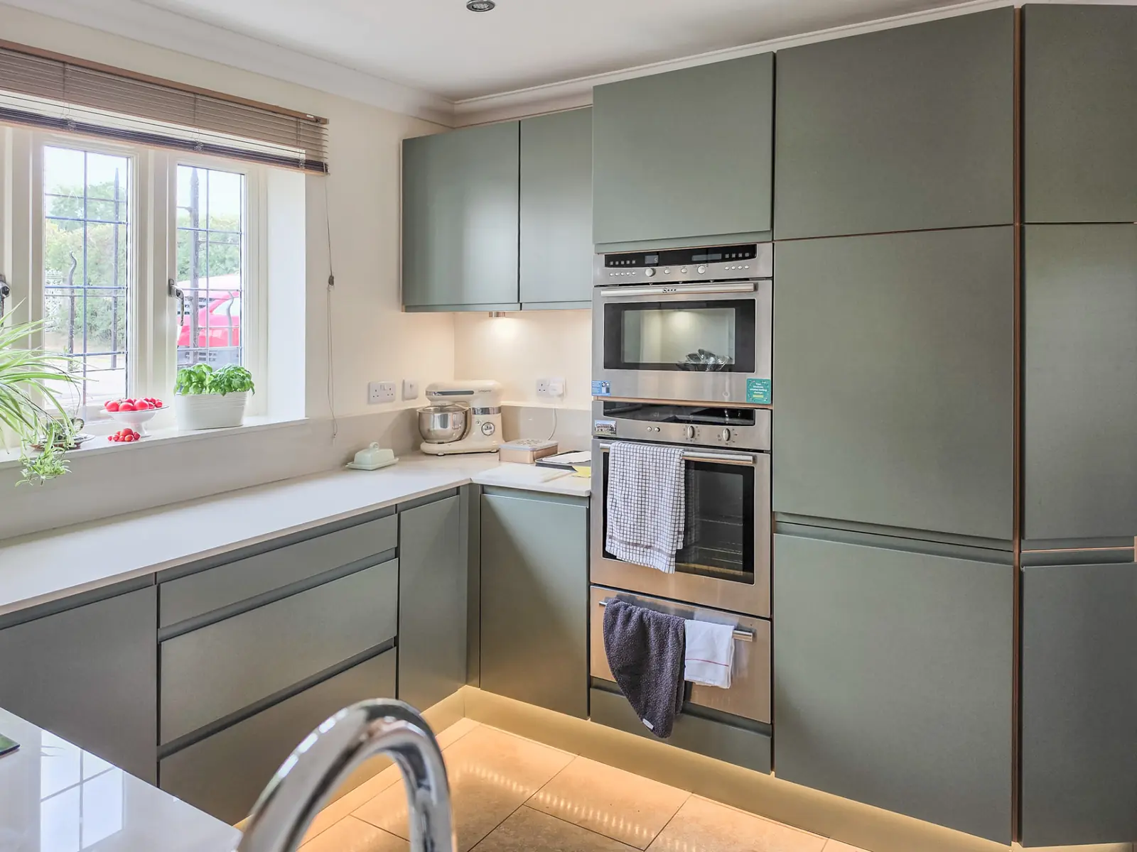 Tall sage green cabinets housing built-in ovens, lit by new LED plinth lighting