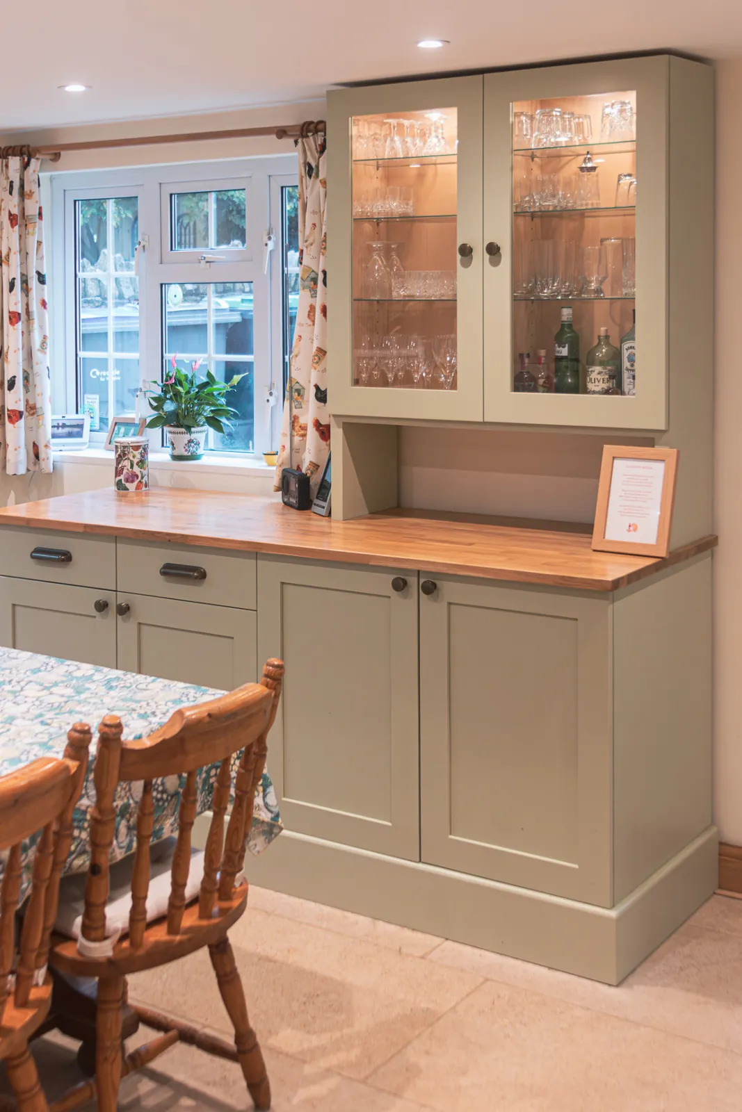 Sage green bespoke kitchen dresser with glazed, lit upper cabinets and an oak worktop