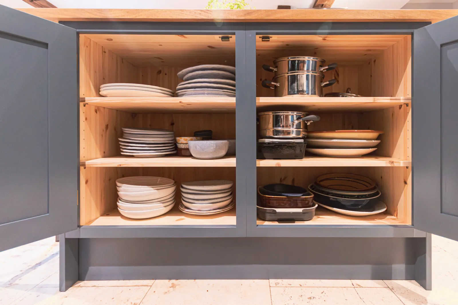 Painted bespoke cabinet doors open to reveal lit timber shelves of plates and cookware