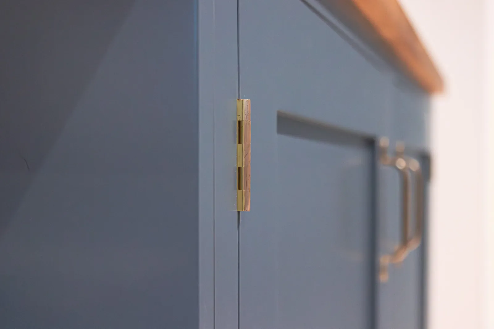 Close-up of a solid brass hinge on a painted bespoke cabinet door