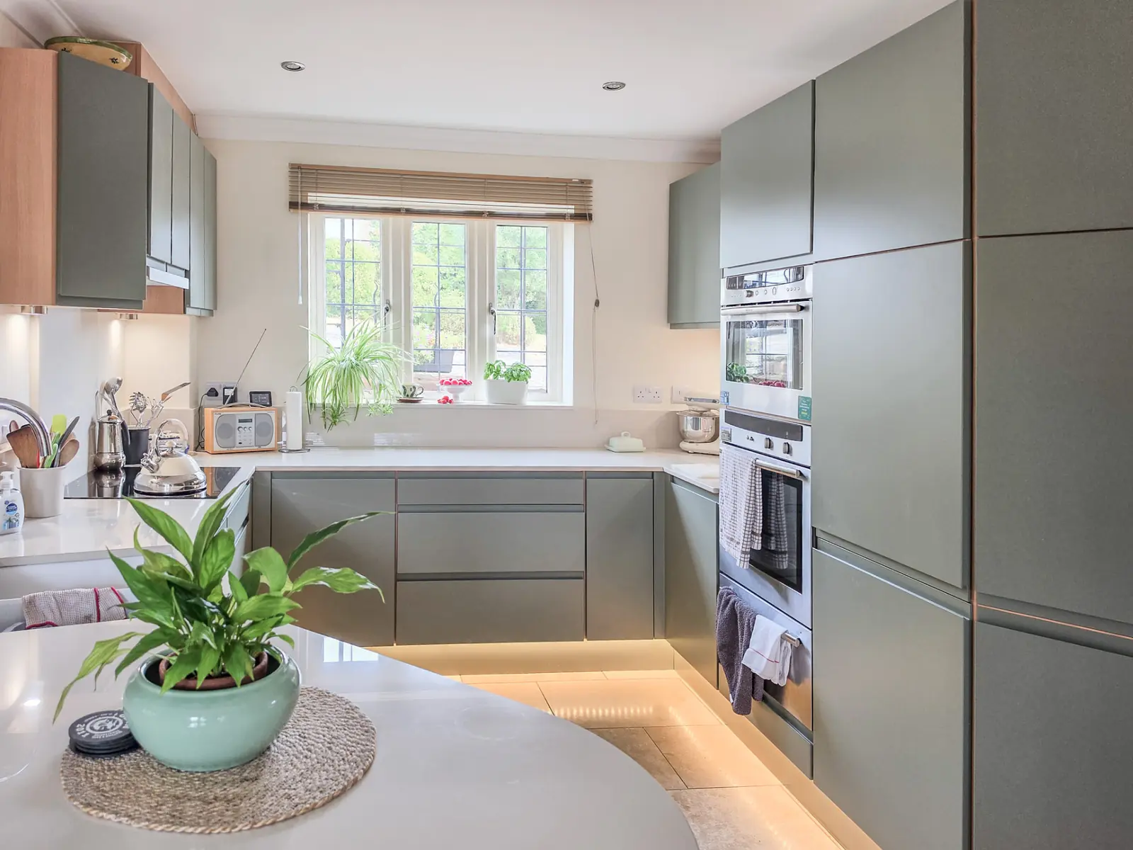 Sage green handleless replacement doors with white Dekton worktops and LED plinth lighting